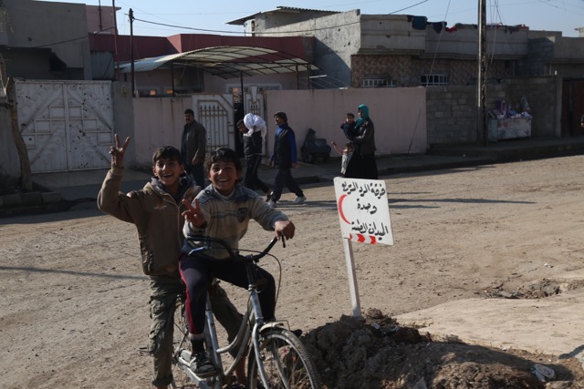 Children give us the victory sign, next to a sign pointing to the Iraqi Army clinic