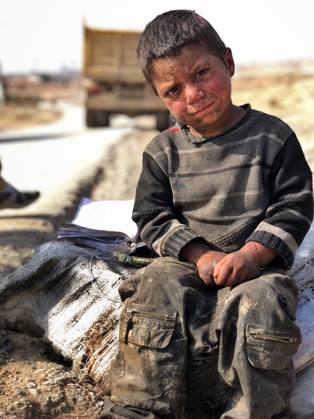 Young boy on the outskirts of Raqqa with his mom and sister, picking through trash.