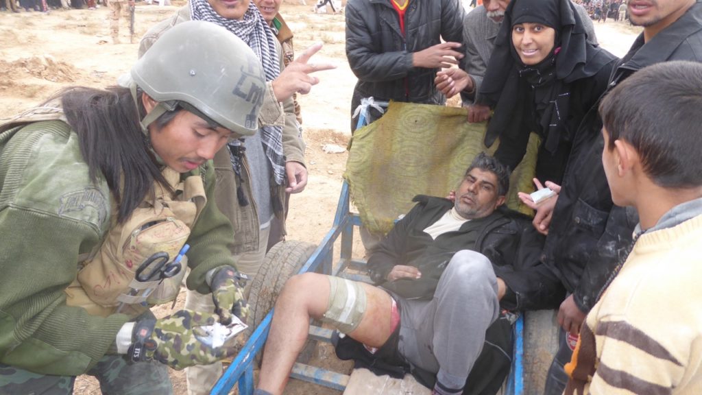 Man who was shot by ISIS as he waited for food being treated by Burma medic Joseph as family keeps his place in the food line