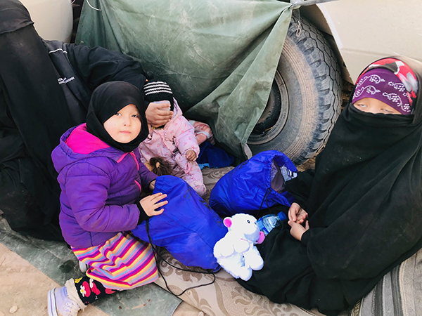 A former ISIS family finds shelter from the wind behind our trucks. 