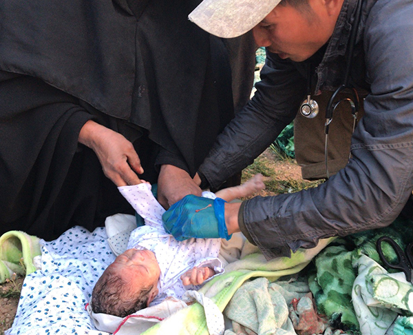 Joseph, a Karen medic, inspects a new baby born in the desert.