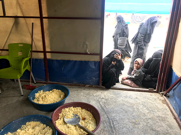 IDP women look into a food prep area at Al-Hol.