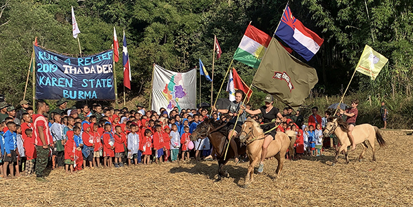 Sahale, Suu, and Peter riding in with the Karen, Kurdish, and SDF flags
