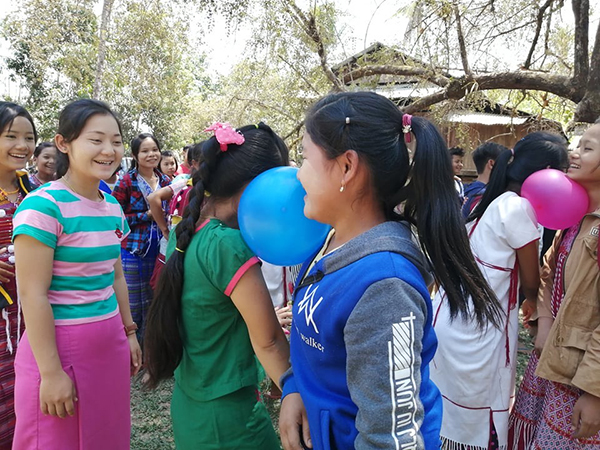 During a Good Life Club program, villagers play a game where they must pop a balloon between their neck and shoulders.