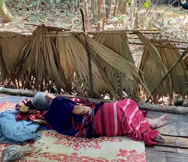 93 year old woman who cannot walk lies on a mat in the jungle
